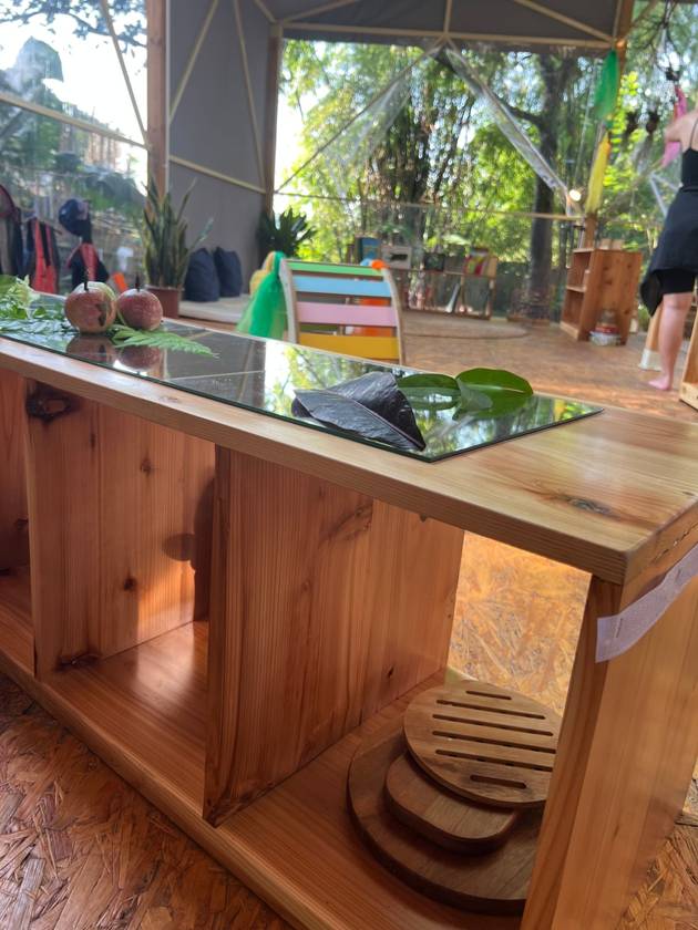 Mirror-topped shelf with leaves and fruit, with the open garden classroom behind it